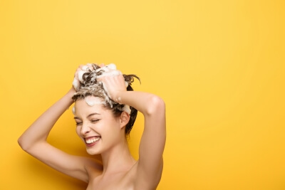 Frau vor gelben Hintergund wäscht Ihre Haare