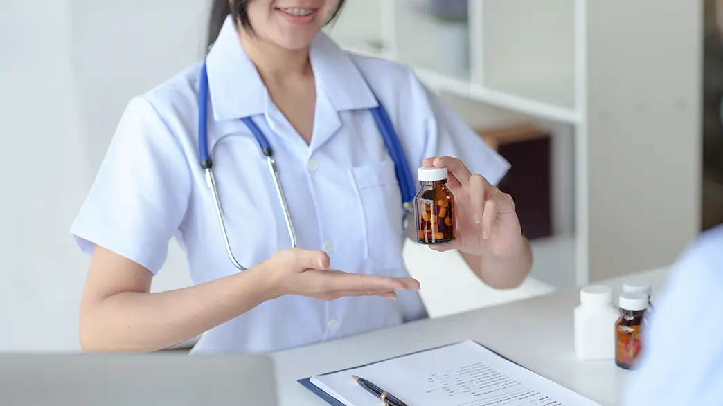 Im Falle einer Arzneimittelallergie lassen sich betroffene Medikamente oft durch alternative Präparate ersetzen Eine junge Ärztin präsentiert an ihrem Schreibtisch ein Gläschen mit Pillen