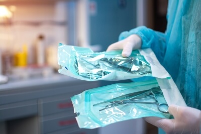 Nahaufnahme eines Zahnarztes, der in einer Schutzfolie verpackte zahnärztliche Werkzeuge hält Steril verpackte zahnärztliche Werkzeuge
