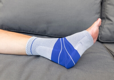 Achillessehnenbandage in Verwendung Fuß mit Achillessehnenbandage auf einer grauen Couch